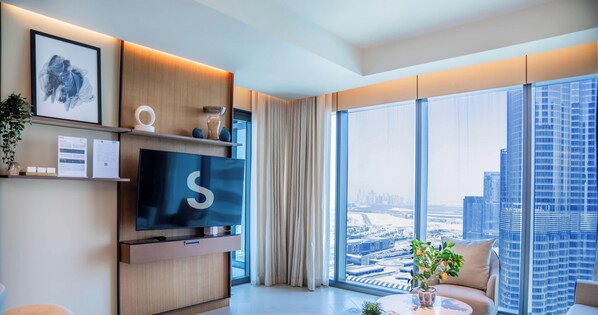 Ein modernes Wohnzimmer mit großem Fernseher, einer Couch, einem Couchtisch und Blick auf die Stadt durch große Fenster.