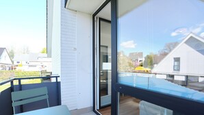 A balcony with a table and chairs, a sliding glass door, and a view of neighboring houses. - House Wendt Apartment 01 (Timmendorfer Strand)