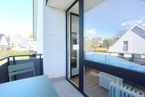 A balcony with a table and chairs, a sliding glass door, and a view of neighboring houses. - House Wendt Apartment 01 (Timmendorfer Strand)