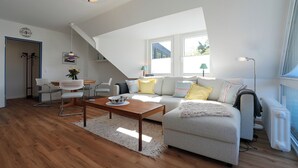 A modern living room with a sofa, coffee table, and chairs, a staircase, and large windows. - House Wendt Apartment 01 (Timmendorfer Strand)