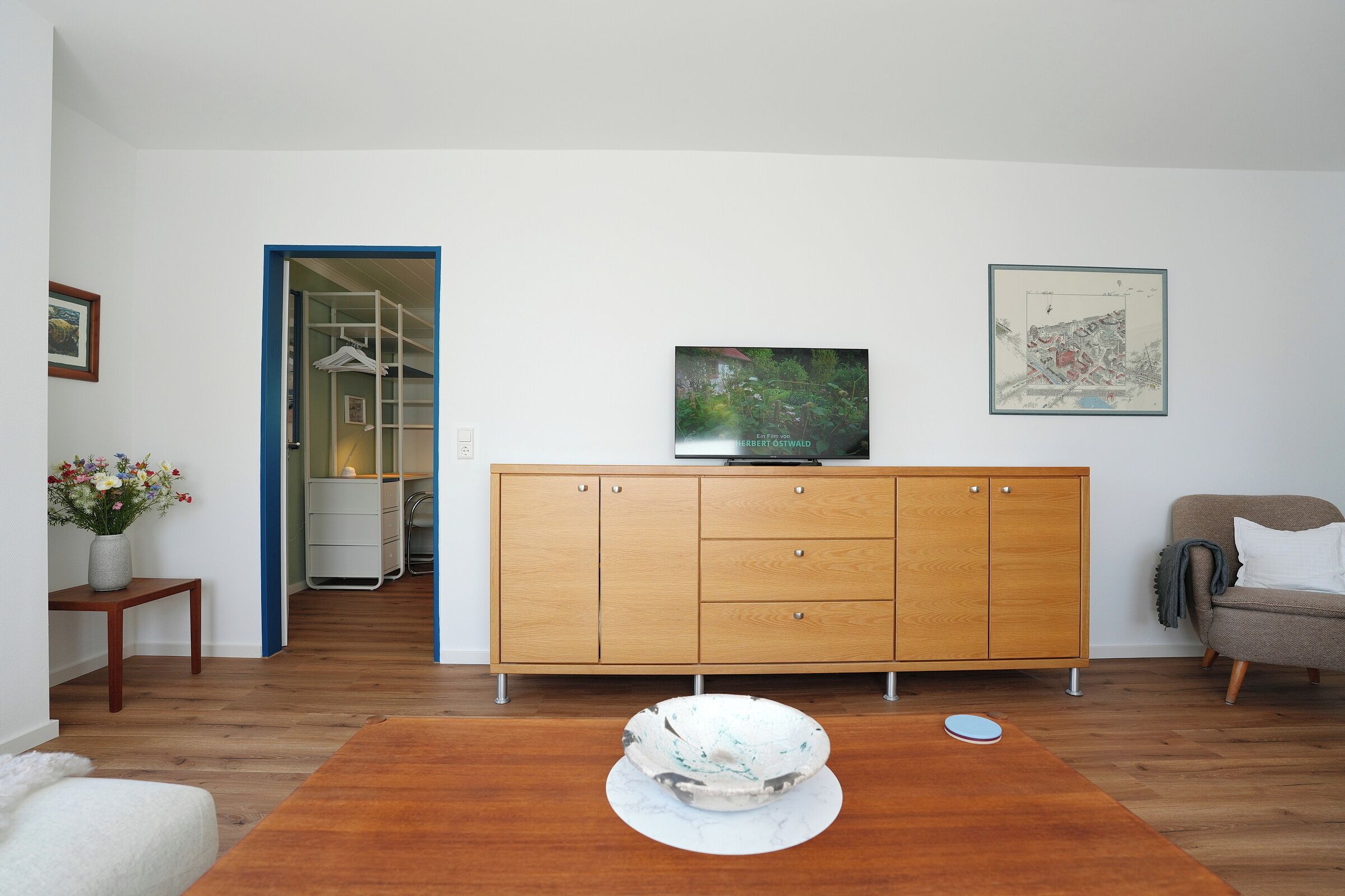 Una sala de estar con un aparador de madera, un televisor, un mapa enmarcado y una silla blanca.