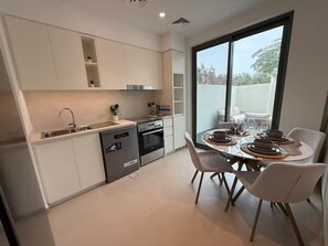 Eine moderne Küche mit integrierten Geräten, ein Essbereich mit Tisch für vier Personen und ein großes Fenster mit Blick ins Freie.