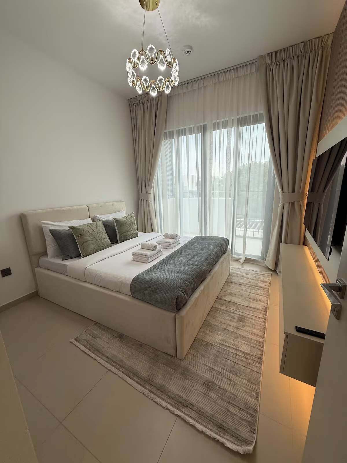 A modern bedroom with a bed, curtains, a television, and a chandelier.