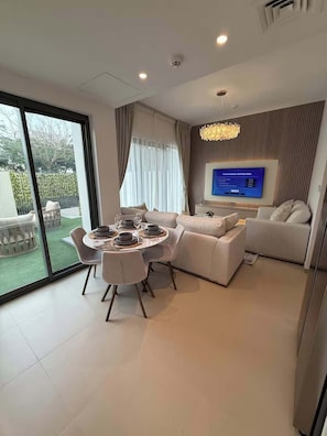 Ein modernes Wohnzimmer mit Essbereich, einem Wand-Fernseher und Blick ins Freie.