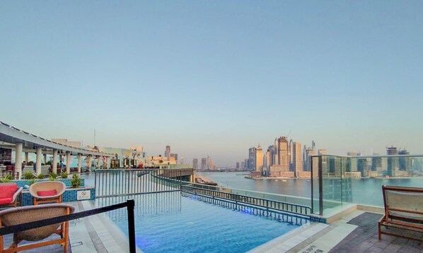 Ein Pool auf dem Dach mit Blick auf die Stadt, Liegestühlen und einer Glasreling.