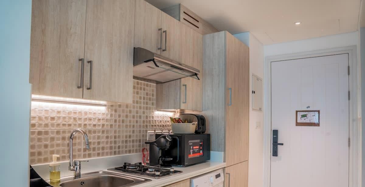 A modern kitchen with wooden cabinets, a gas stove, a coffee machine, and a tiled backsplash.