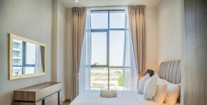Ein Schlafzimmer mit großem Fenster, Nachttisch, Bett mit Kissen und einem Spiegel an der Wand.