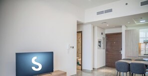 Ein modernes Wohnzimmer mit Flachbildfernseher, einem Essbereich mit Tisch und Stühlen sowie einer sichtbaren Badezimmertür.