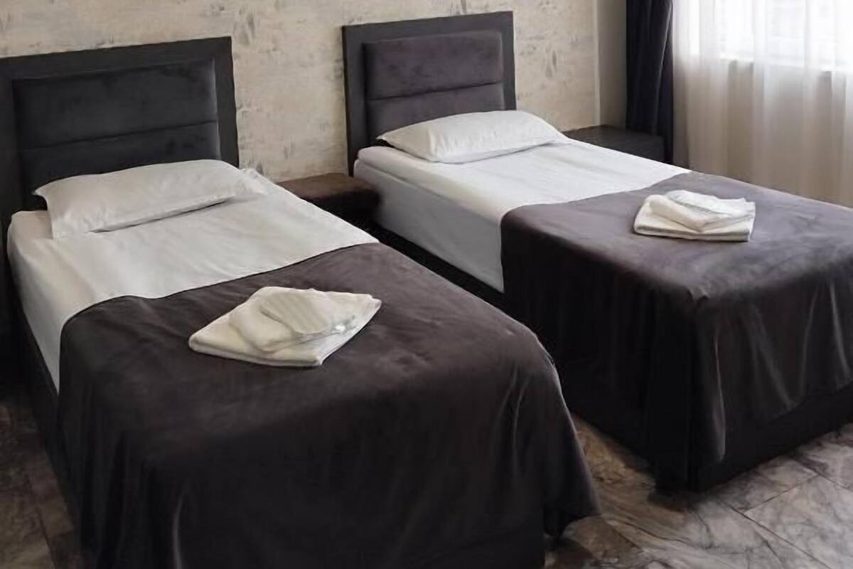Una habitación con dos camas, una ventana con cortinas y una pared con textura.
