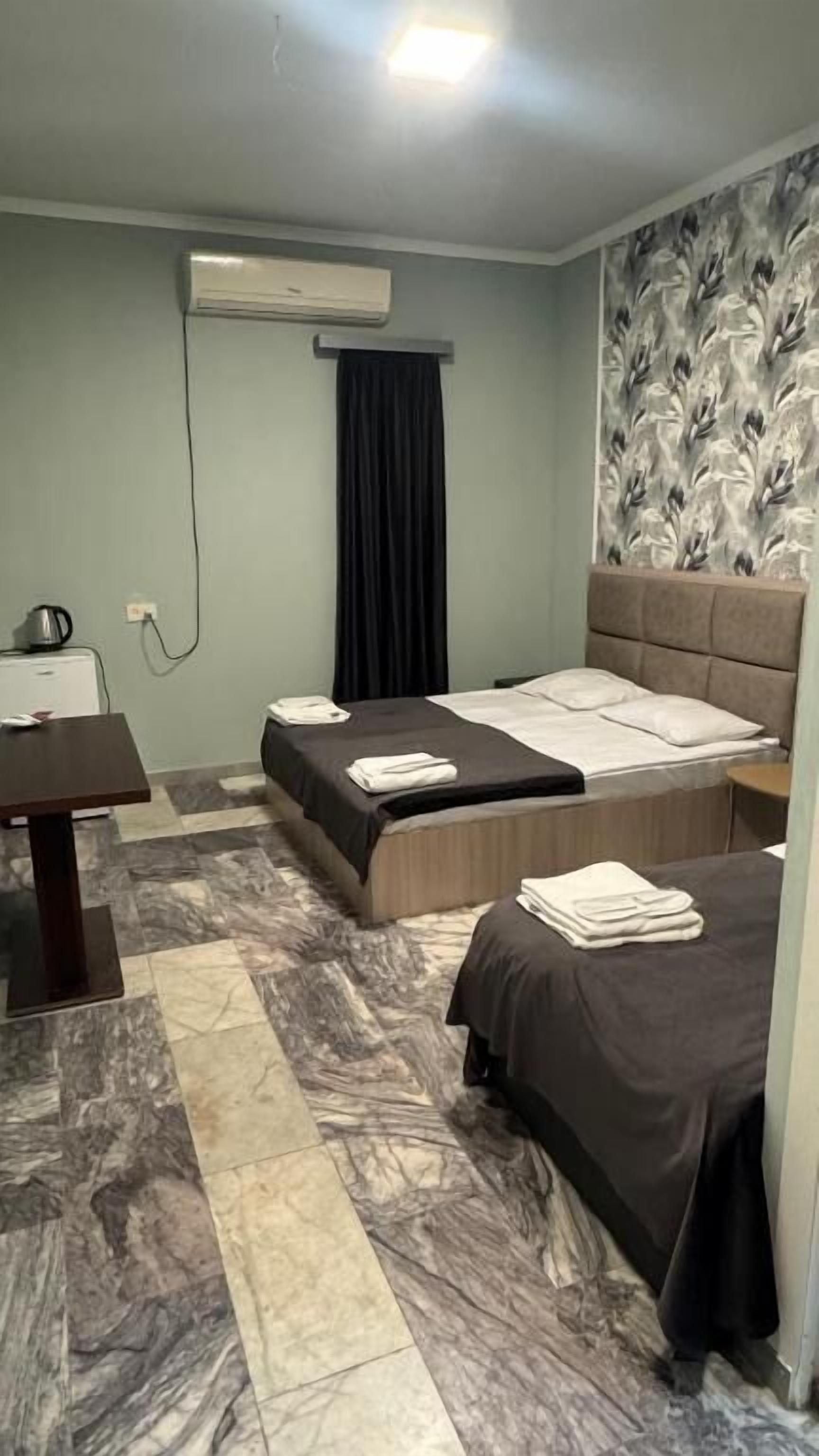Habitación de hotel con dos camas, un escritorio, una silla, aire acondicionado y una pared con diseño.