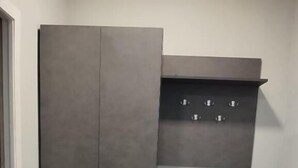 A room with a grey wardrobe, a small shelf, and a trash bin. - Corner Hotel  (Yerevan)