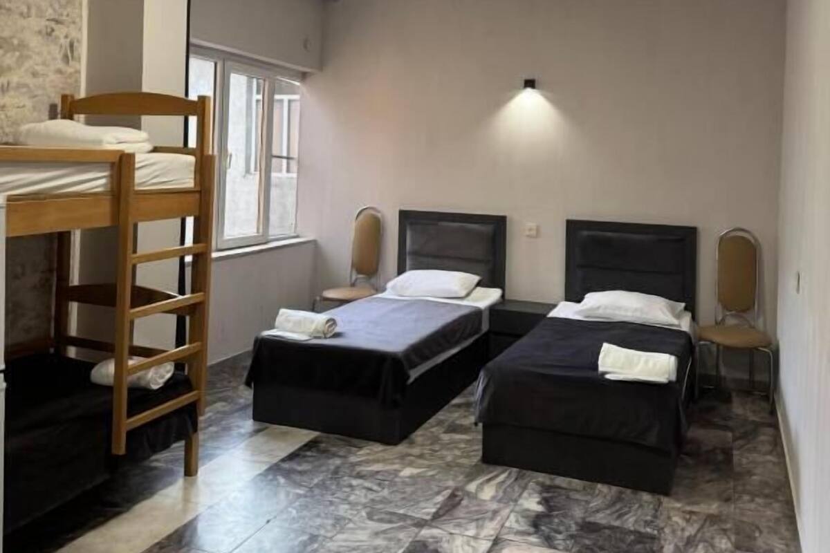 Una habitación con dos camas, una litera, una ventana y una lámpara fijada a la pared.