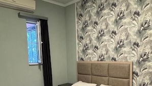 A bedroom with a bed, a headboard, a nightstand, a window, and a wall with a floral pattern. - Corner Hotel  (Yerevan)