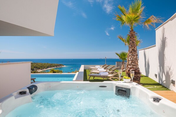 Ein Whirlpool mit Meerblick, Liegestühle und eine Palme.
