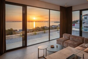 Ein modernes Wohnzimmer mit großem Fenster und Blick auf einen Sonnenuntergang.