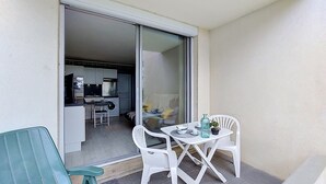 Ein Balkon mit Tisch und Stühlen, eine Glastür zu einer Küche und ein kleiner Blumentopf.