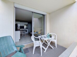 Ein Balkon mit Tisch und Stühlen, eine Glastür zu einer Küche und ein kleiner Blumentopf.