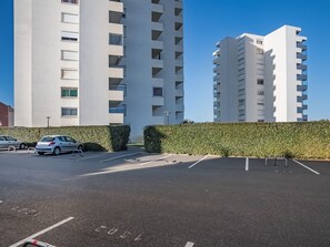 Ein Parkplatz mit zwei weißen Mehrfamilienhäusern im Hintergrund.