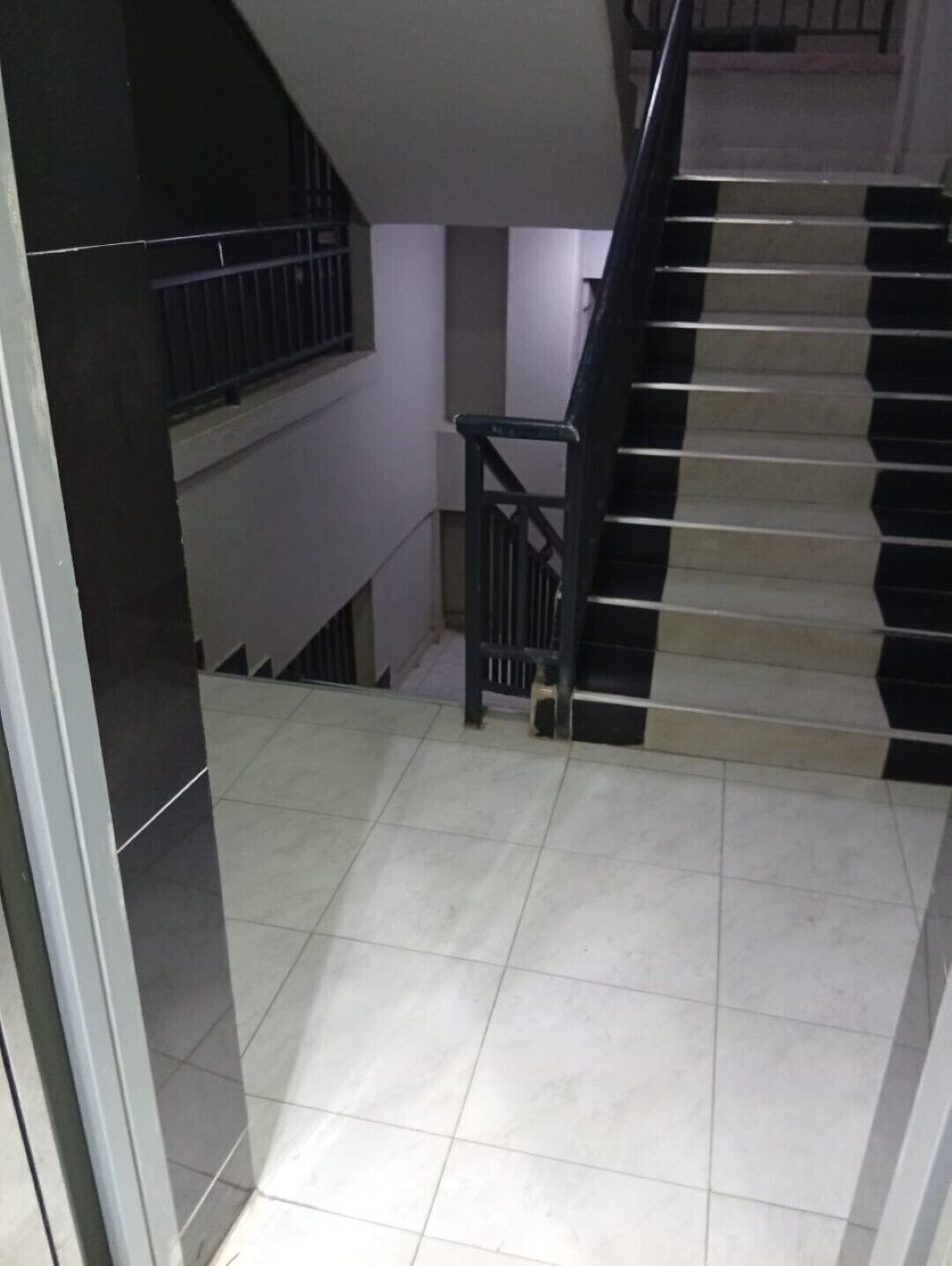 A staircase with black and white steps, a metal railing, and a tiled floor.