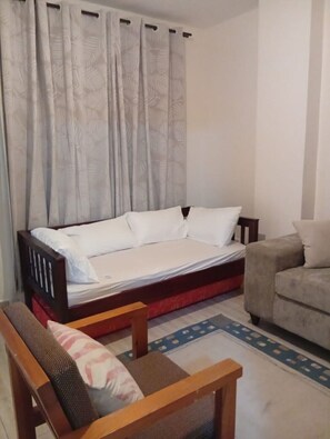 Um quarto com cama, um banco de madeira, um sofá e uma cortina estampada.