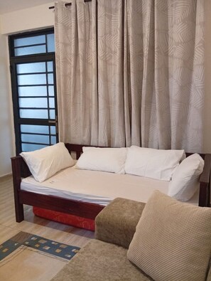 Ein Schlafzimmer mit einem Bett, einem Fenster mit schwarzem Rahmen und einem Vorhang.