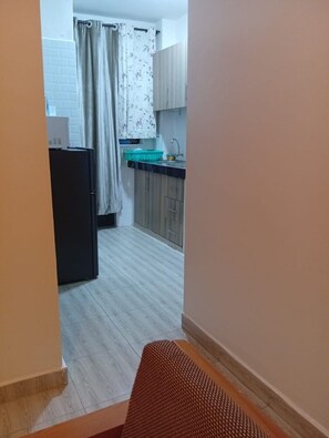 Ein enger Gang führt zu einer Küche mit Kühlschrank, Spüle und Schränken.
