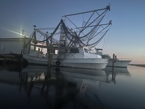 En stillastående fiskebåt låg förtöjd vid en brygga, och det lugna vattnet speglade byggnadens konturer.