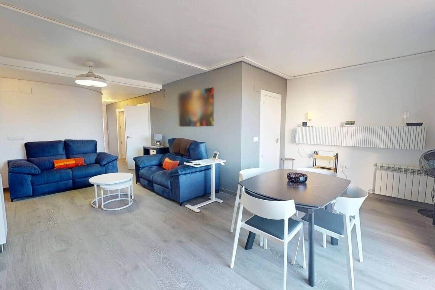 Una sala de estar moderna con sofá, una mesa de comedor con sillas, una mesita auxiliar y un ventilador de techo.