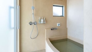 A modern bathroom with a freestanding bathtub, a handheld showerhead, and a small window.