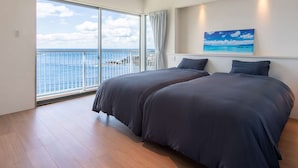 A bedroom with two beds, a large window with a view of the sea, and a painting on the wall.