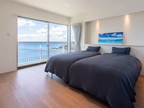 Une chambre avec deux lits, une grande fenêtre donnant sur la mer et un tableau accroché au mur.