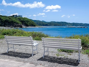 Two white benches on a gravel path with a view of a coastal landscape, including a body of water and distant hills.