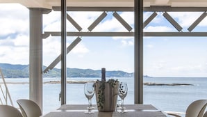 A dining area with a table set for four, overlooking a body of water with mountains in the distance.