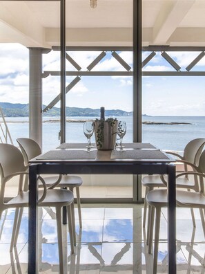 Un coin repas avec une table dressée pour quatre personnes, donnant sur une étendue d’eau et offrant une vue sur des montagnes au loin.