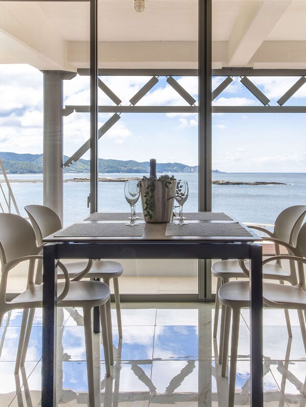 Un coin repas avec une table dressée pour quatre personnes, donnant sur une étendue d’eau et offrant une vue sur des montagnes au loin.