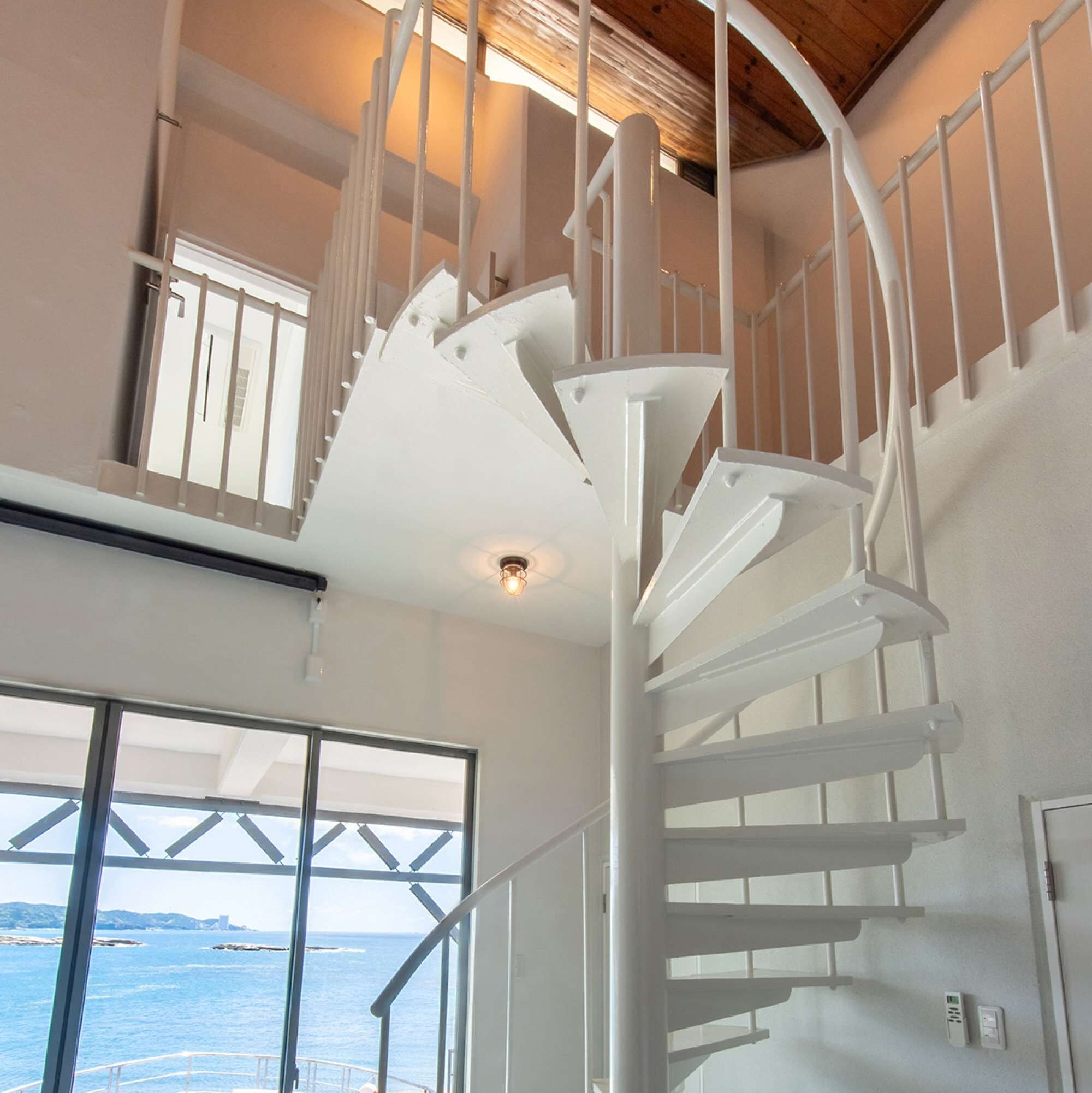 A white spiral staircase in a room with large windows overlooking a body of water.