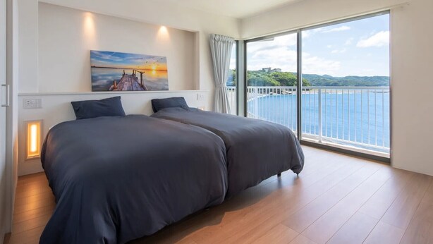 Une chambre avec deux lits, un tableau, une grande fenêtre donnant sur la mer et un balcon.