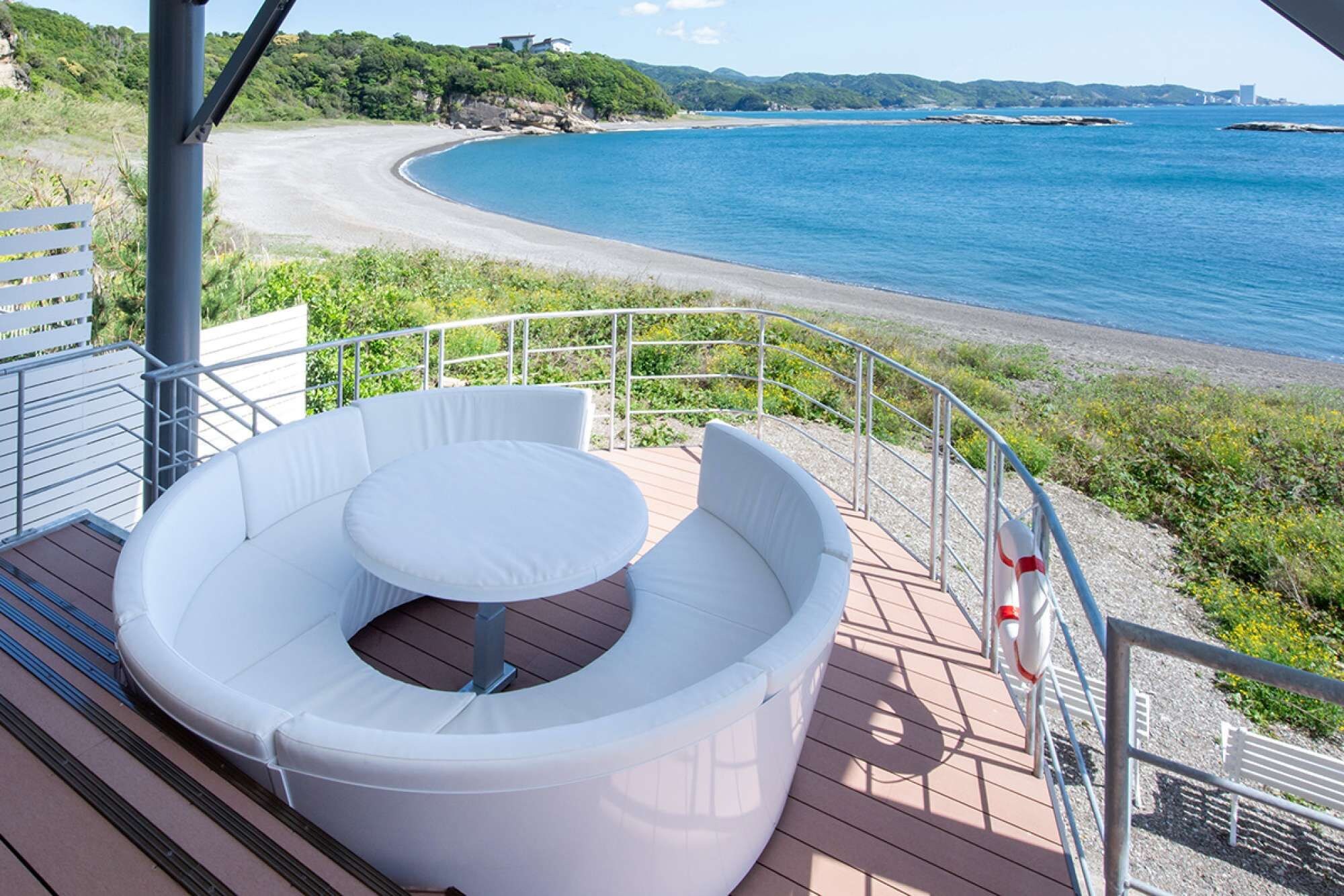A deck with a circular seating area overlooking a beach and the sea.