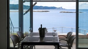 Une table avec quatre chaises, une bouteille de champagne et deux verres à vin, le tout sur un balcon offrant une vue sur la mer et le paysage lointain.
