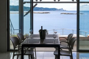 A table with four chairs, a bottle of champagne, and two wine glasses on a balcony with a view of the sea and distant land. - Private Villa Kai -KUMANO- Have the sky and the sea all to yourself. That's the only luxury. (Shirahama-cho)