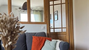 Een woonkamer met een bank, een ronde houten tafel en een vaas met gedroogde bloemen.