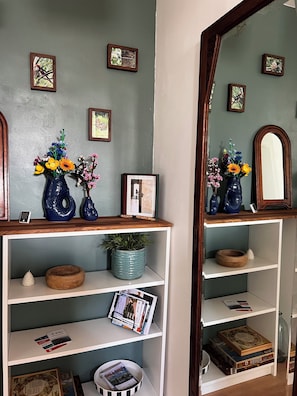 A room with a wooden shelf displaying books, a vase with flowers, and framed pictures on the wall. - 10° Ouest - T3 renovated 2025 - Park view - Quiet street (Lorient)