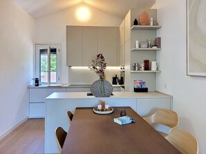 Une cuisine moderne dotée d’un îlot central, de meubles blancs et d’un coin repas avec une table et des chaises marron.