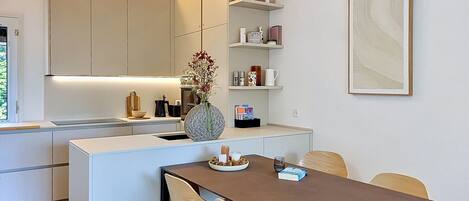 Una cucina moderna con isola centrale, un tavolo da pranzo con sedie e un ripiano a parete con oggetti decorativi.