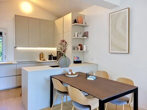 Une cuisine moderne dotée d’un îlot central, d’une table à manger avec des chaises, et d’une étagère murale agrémentée d’objets décoratifs.