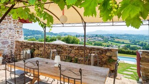 A stone wall, a wooden table, and metal chairs in an outdoor setting with a view of a valley.