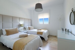 A bedroom with two beds, a bedside table, a lamp, a window, and a mirror. - 3-Bedroom Apartment with Panoramic Sea Views | La Cala de Mijas (La Cala de Mijas)