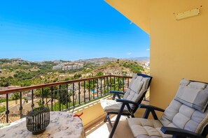 A balcony with two chairs, a table, and a view of a hilly landscape. - 3-Bedroom Apartment with Panoramic Sea Views | La Cala de Mijas (La Cala de Mijas)