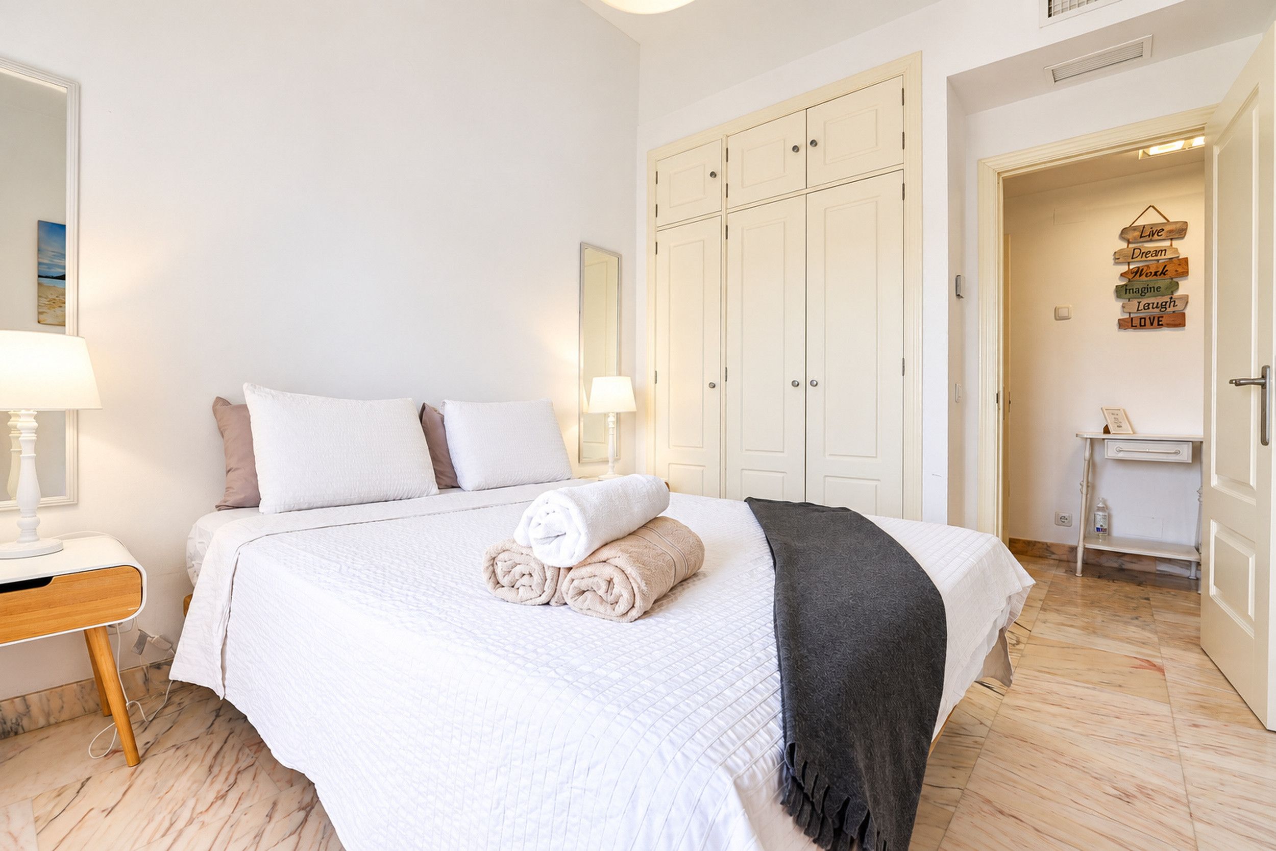 Una camera d'albergo con un letto, un comodino, uno specchio, un armadio e una porta con un cartello motivazionale.