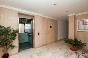 A hallway with an elevator, a door with a sign, and potted plants. - 3-Bedroom Apartment with Panoramic Sea Views | La Cala de Mijas (La Cala de Mijas)